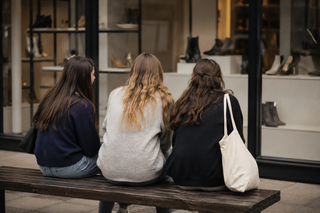 girls sitting on a bench looking a shoe shop window