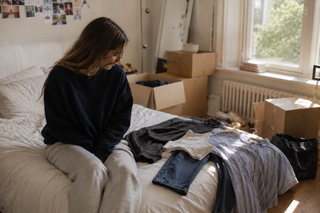Young woman choosing an outfit in her half-packed bedroom before leaving for university.