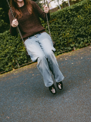 Teenage girl on a swing in a brown cable-knit jumper, light-wash jeans and black soft crinkled patent Maévie Oxford Ballet flats
